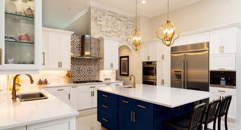 Large white kitchen with gorgeous marble counter island and dark blue cabinets underneath.
